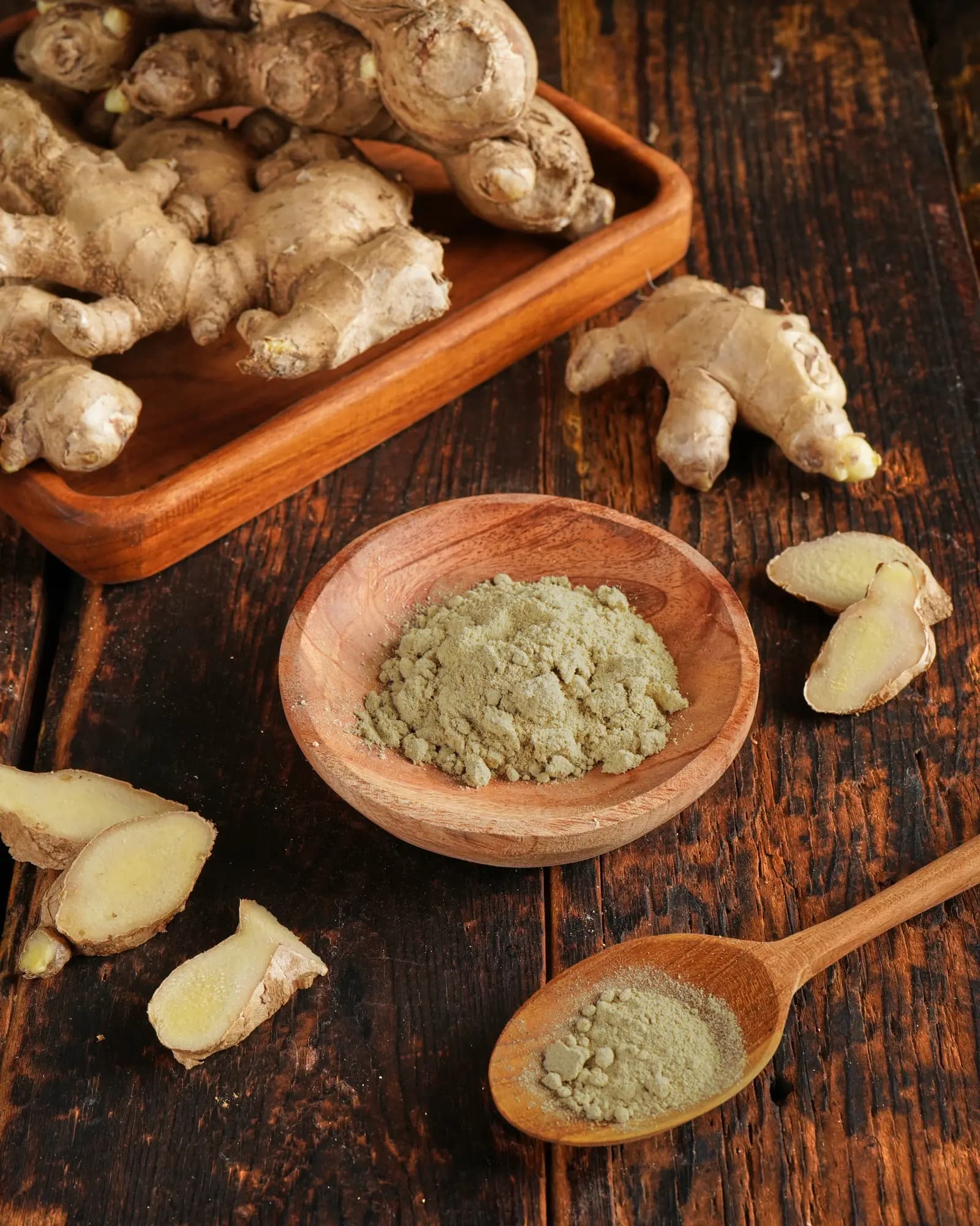 Ground Jahe Gajah powder in a wooden bowl with fresh rhizomes alongside